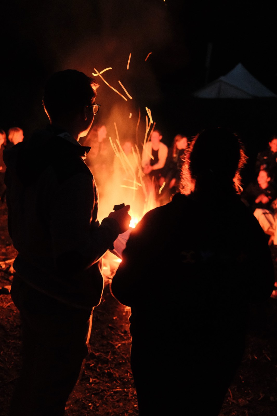 Zwei Silhouetten am Lagerfeuer, Funken steigen in die Nacht