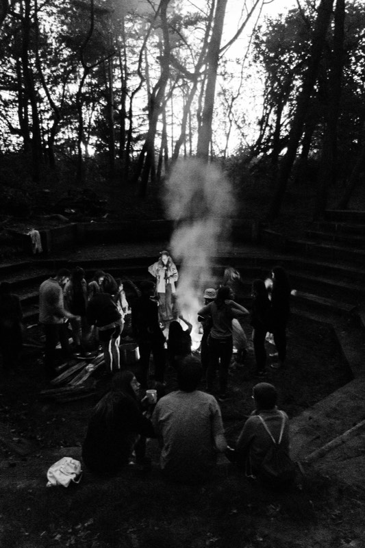 Menschen sitzen in der Dämmerung im Kreis um ein Lagerfeuer im Wald
